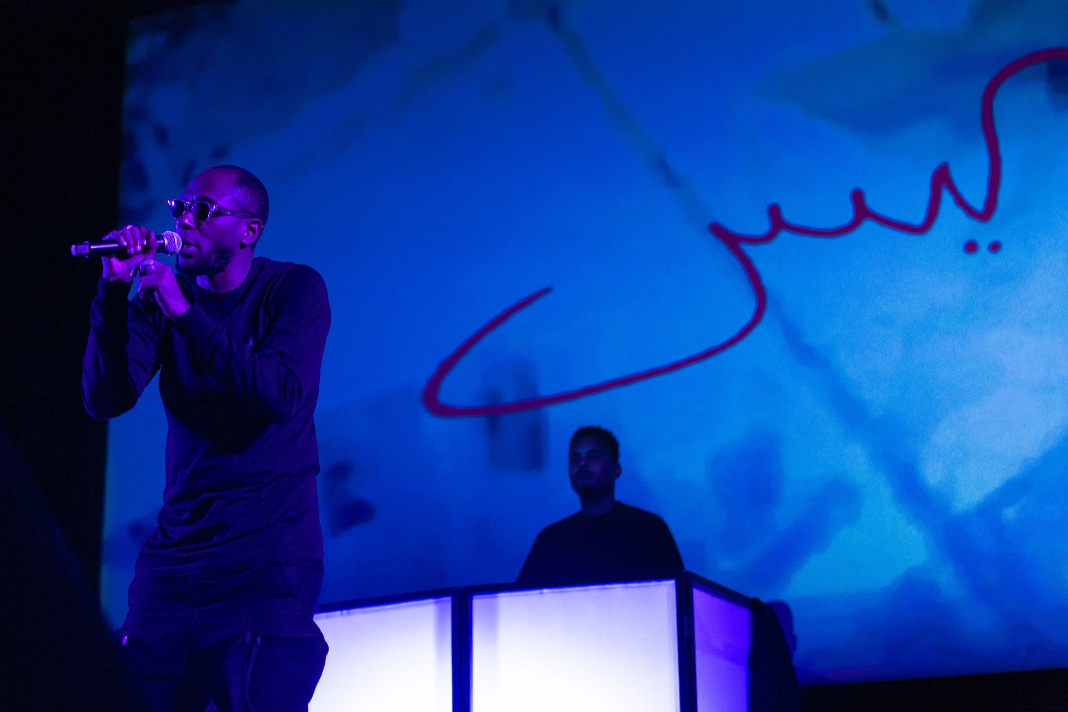Yasiin Bey performing in blue projection light with Lord Tusk at Brooklyn Museum