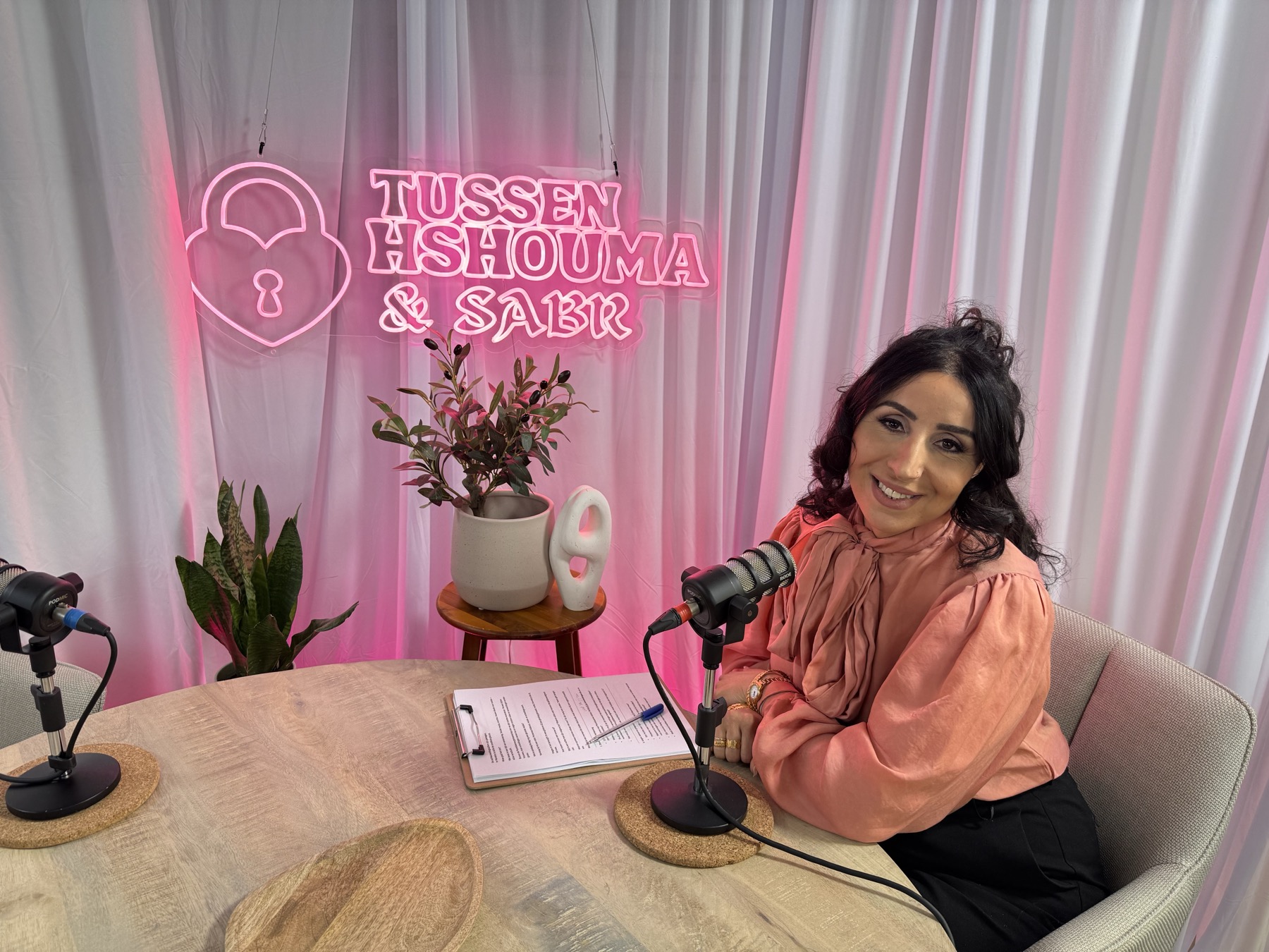 Host seated by neon podcast sign